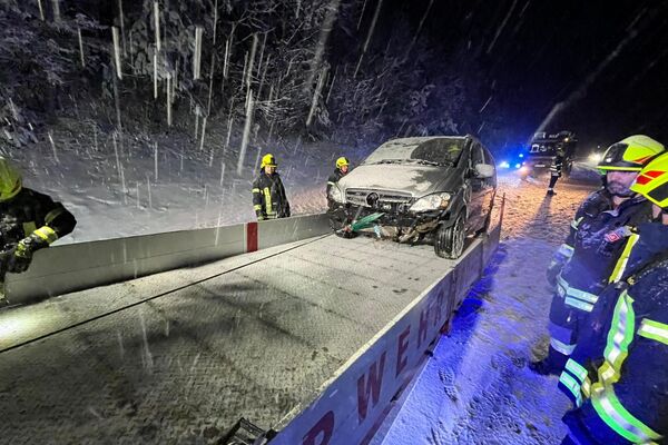 Feuerwehrleute bergen ein Auto auf einer verschneiten Straße bei Nacht. | © Name