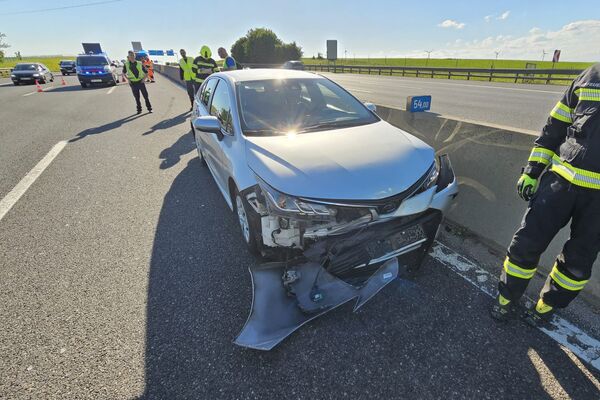 Ein silbernes Auto mit einem Unfallschaden steht an der Autobahn, während Rettungskräfte eingreifen.