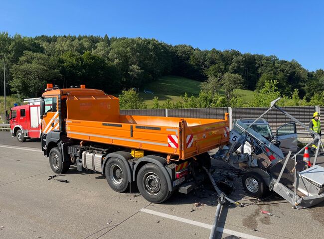 Ein orangefarbener Lkw steht an einer Unfallstelle mit einem beschädigten Auto auf der Autobahn. | © Name