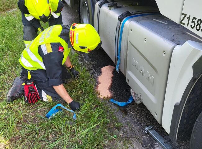 Zwei Feuerwehrmänner untersuchen den Boden neben einem Lkw und reinigen eine ausgelaufene Substanz. | © Name