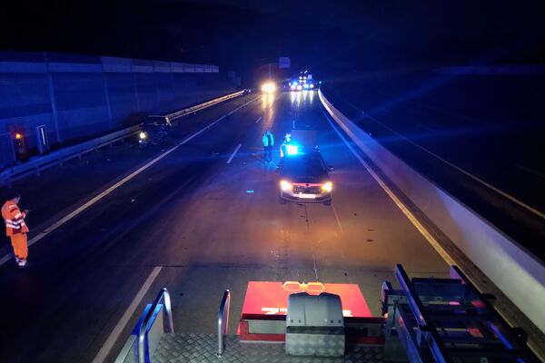 Ein Polizeiauto mit Blaulicht steht auf der Autobahn, während ein Rettungsdienst im Einsatz ist.