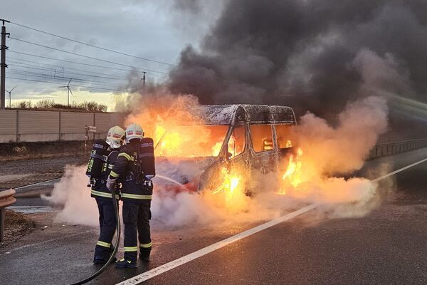 Feuerwehrleute löschen ein brennendes Fahrzeug auf der Straße, während Rauch und Flammen aufsteigen. | © Name