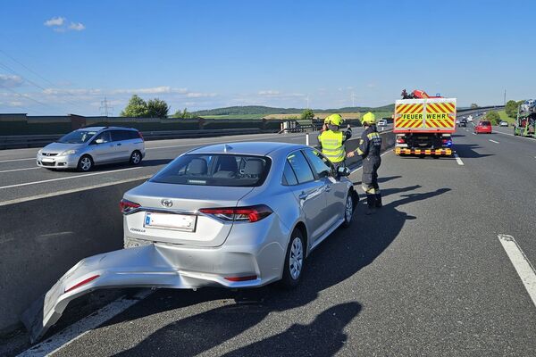 Ein beschädigtes Auto steht auf der Autobahn, während Feuerwehrleute den Vorfall untersuchen. | © Name