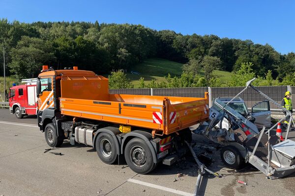 Ein orangefarbener Lkw steht an einer Unfallstelle mit einem beschädigten Auto auf der Autobahn. | © Name