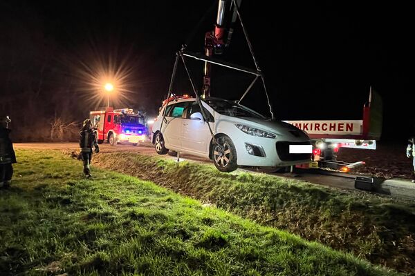 Ein Feuerwehrfahrzeug hebt ein Auto mit einem Kran in der Nacht an einer Landstraße. | © Name