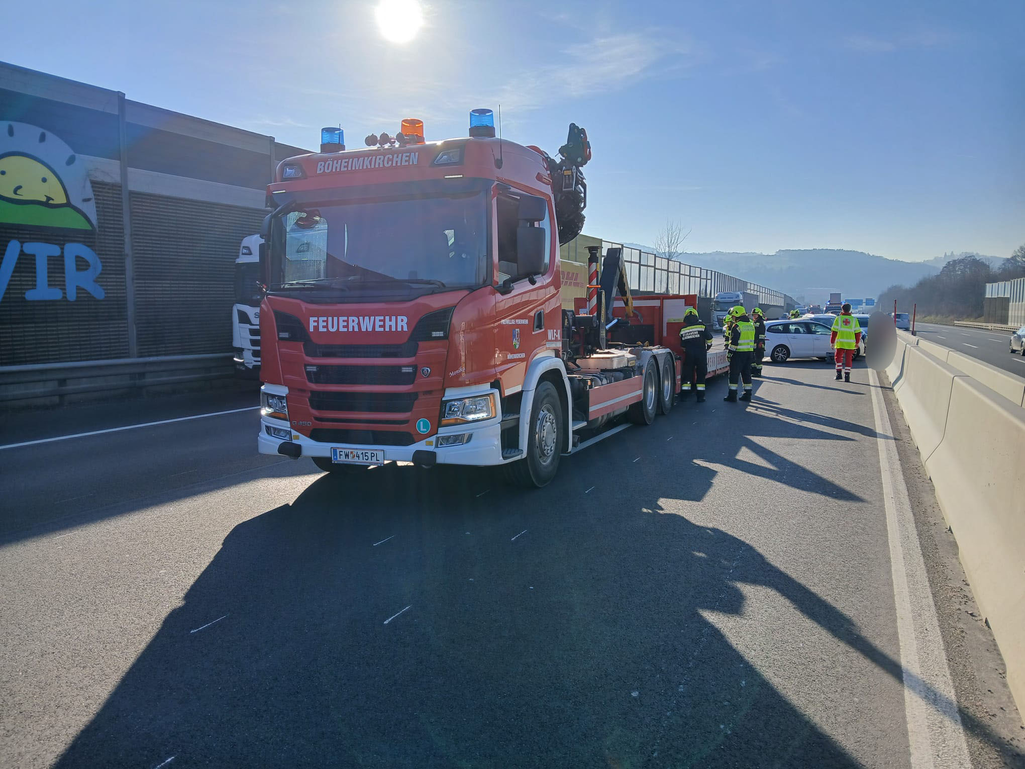 Ein Feuerwehrfahrzeug steht an einer Autobahn, während Rettungskräfte einen Unfallort sichern. | © Name