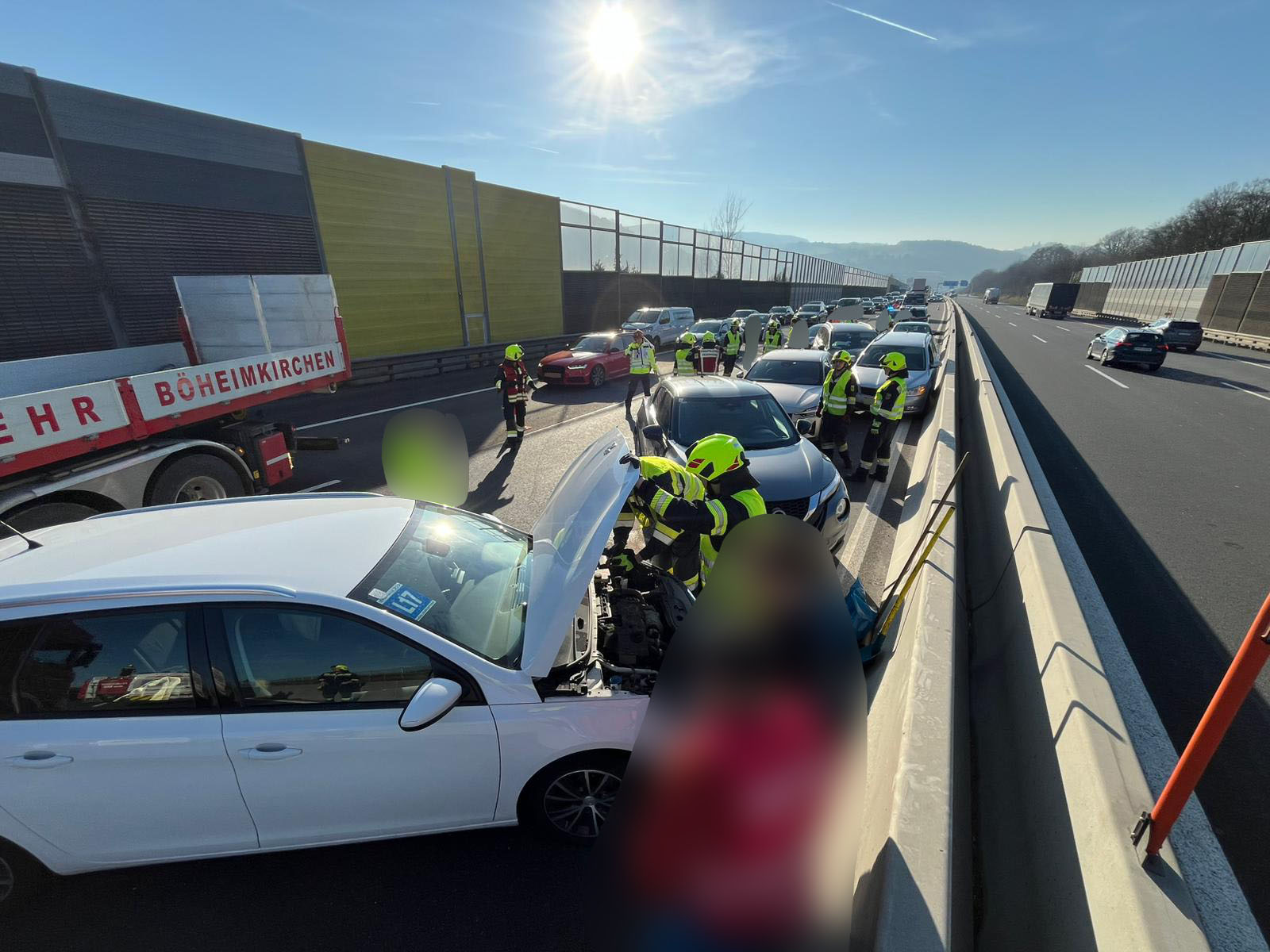 Rettungskräfte untersuchen ein Fahrzeug auf der Autobahn bei Sonnenlicht, während der Verkehr stockt.