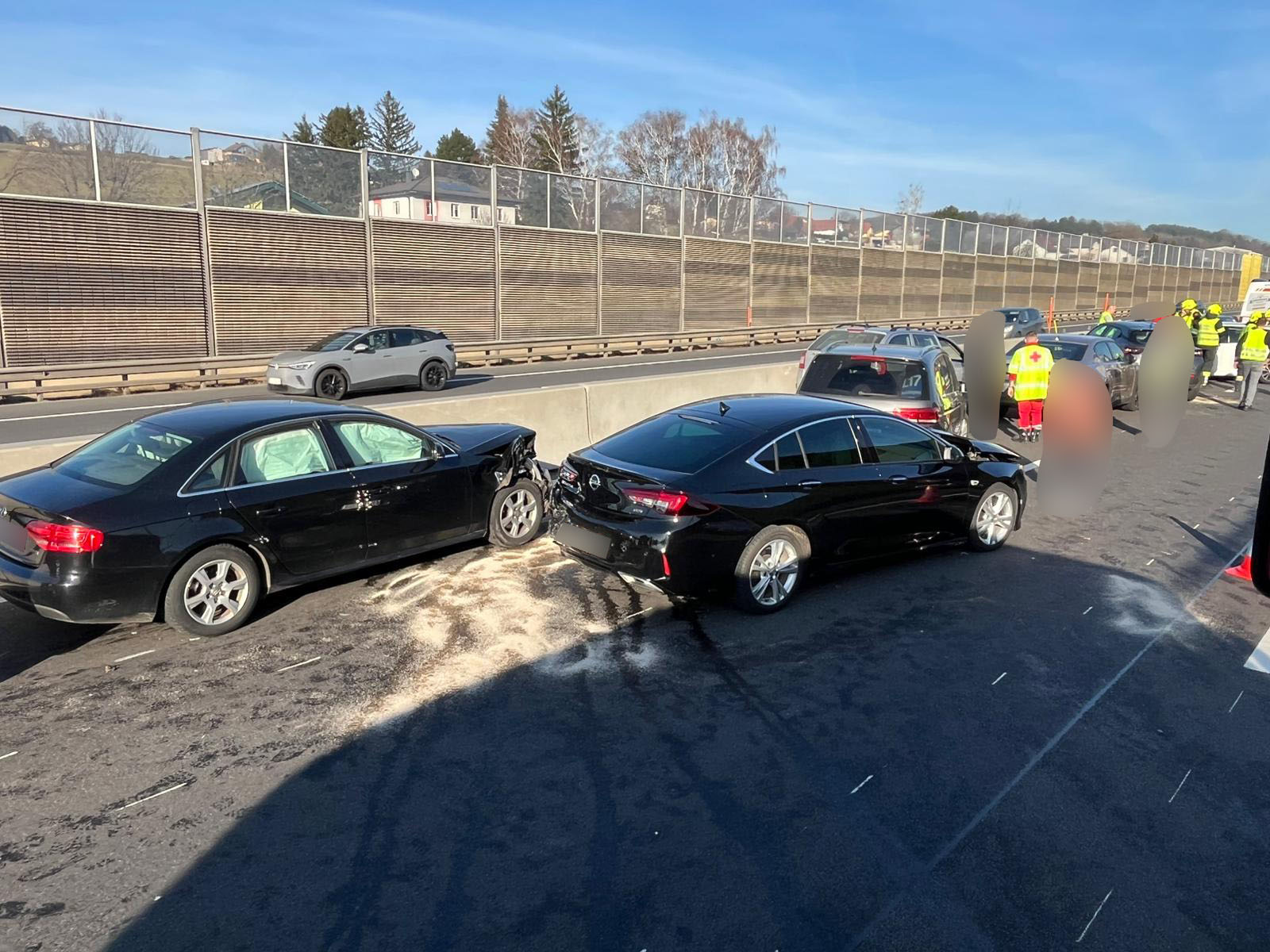 Zwei beschädigte Autos nach einem Verkehrsunfall auf der Autobahn, mit Einsatzkräften im Hintergrund.